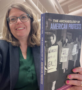 Dr. April M. Beisaw holding a copy of her co-authored book The Archaeology of American Protests
